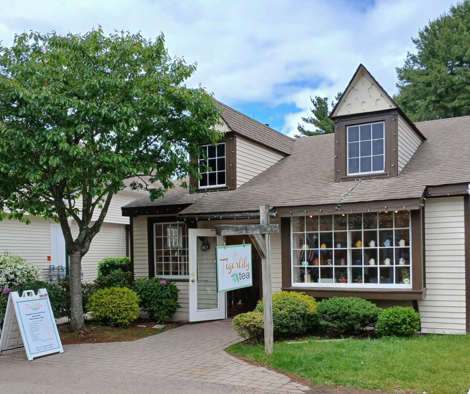 House with a sign outside, surrounded by trees and a clear sky
