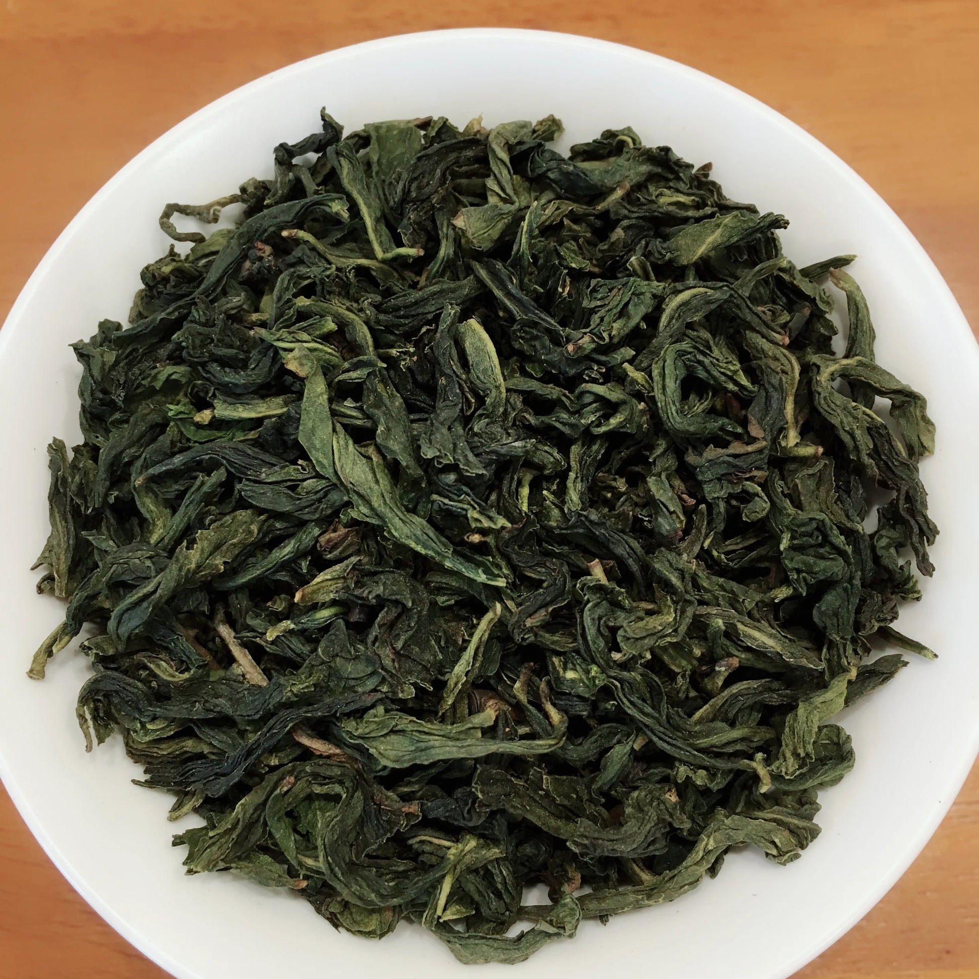 Dry green tea leaves on a white plate with a wooden background