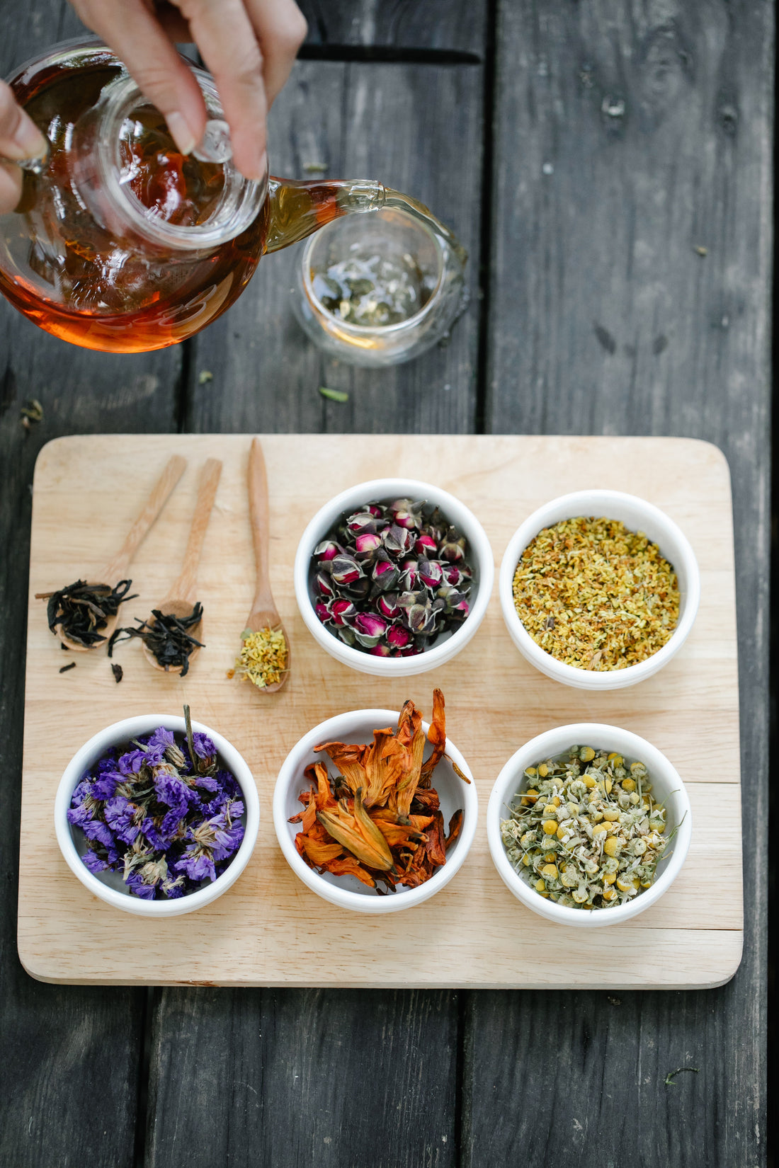 Tea-making setup with dried tea leaves and a person pouring tea into a glass.