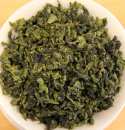 Close-up of green tea leaves in a white bowl on a wooden surface