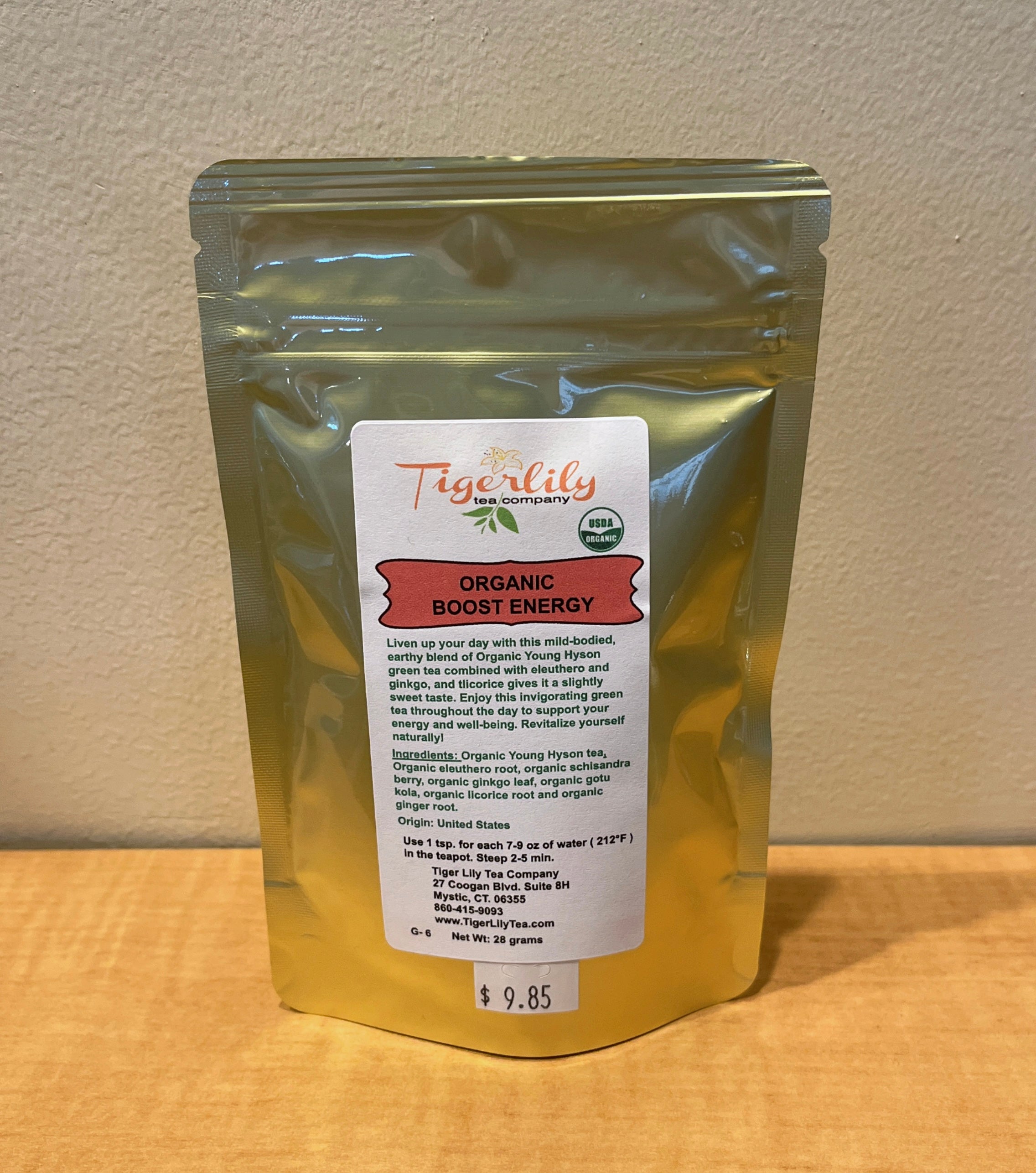 Gold packaging of Tiger Lily Organic Boost Energy on a wooden surface with a beige wall background