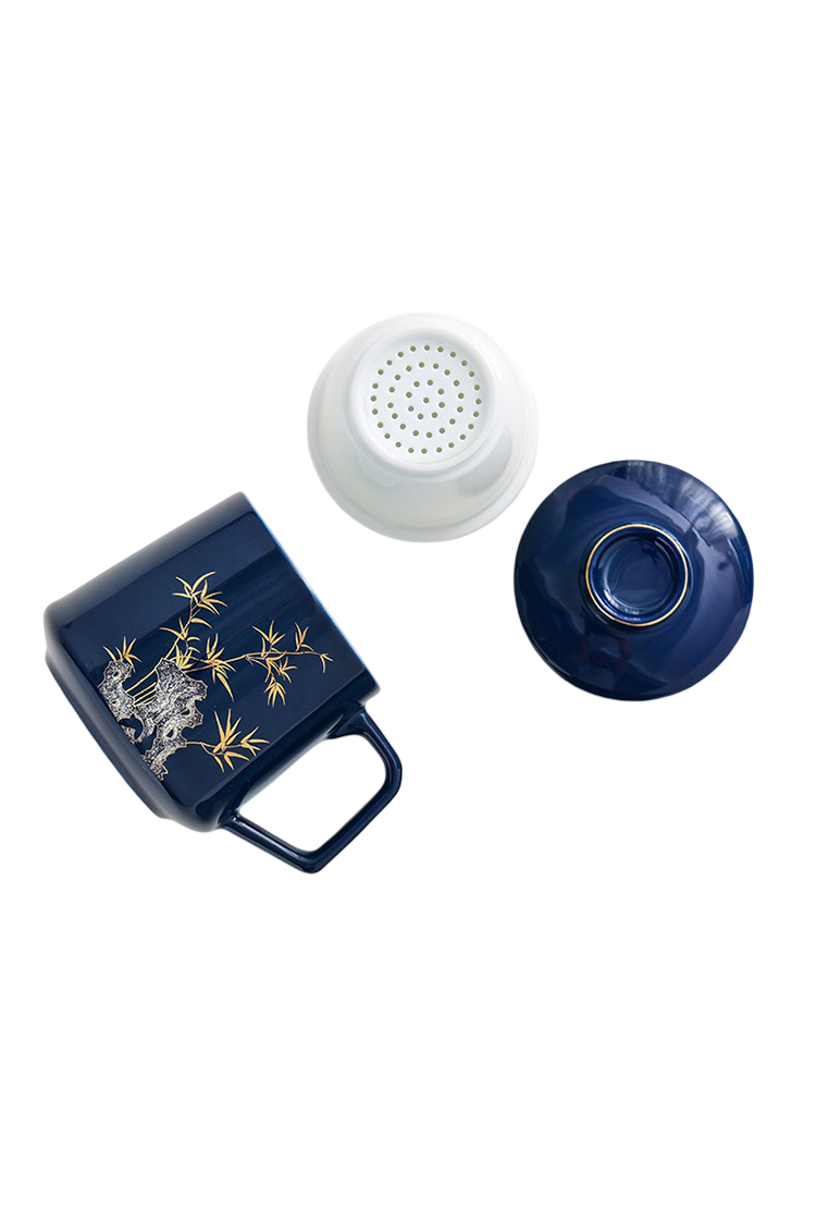 Navy blue mug with gold designs, white strainer, and blue lid on a white background