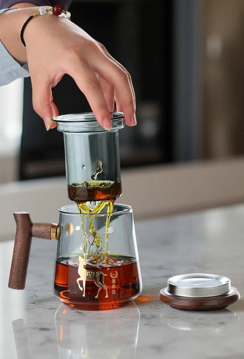 Glass teapot with wooden handle on a marble surface, hand pouring tea.