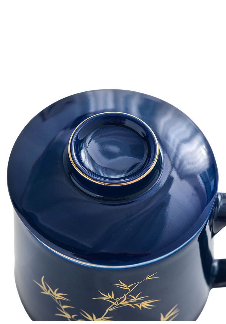 Blue ceramic mug with lid and gold bamboo design on a white background