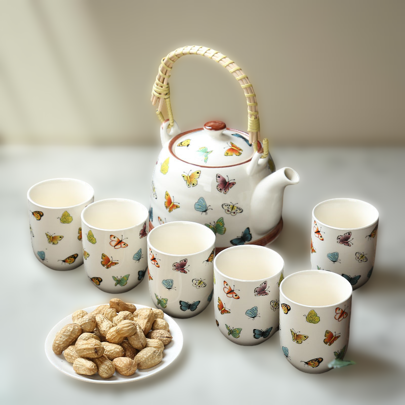 Tea set with teapot and cups featuring butterfly designs on a light surface.