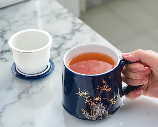 Navy blue mug with floral design held by a hand, filled with tea, on a marble surface.