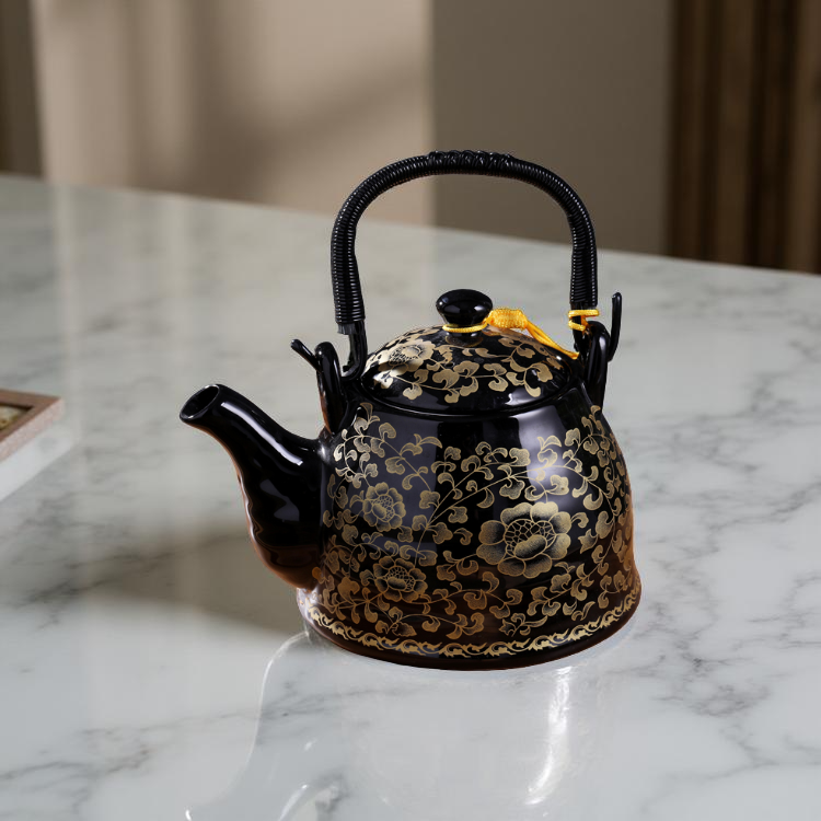 Black teapot with gold floral patterns on a marble surface