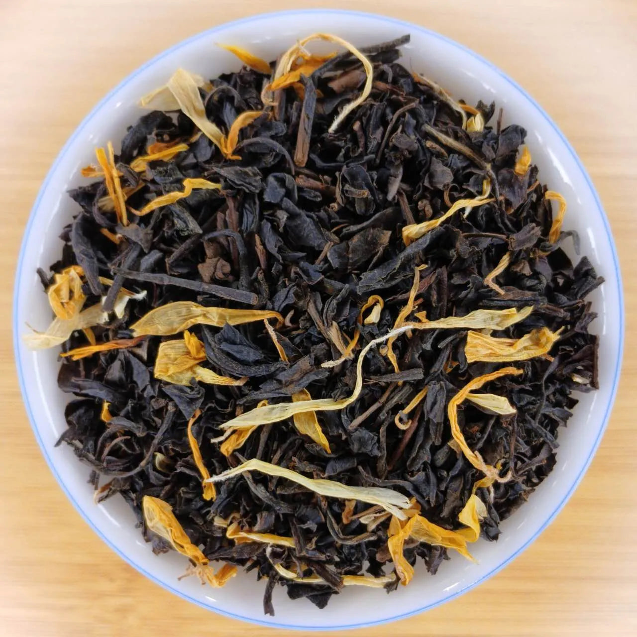 Dried black tea leaves with orange peel in a white bowl on a wooden surface