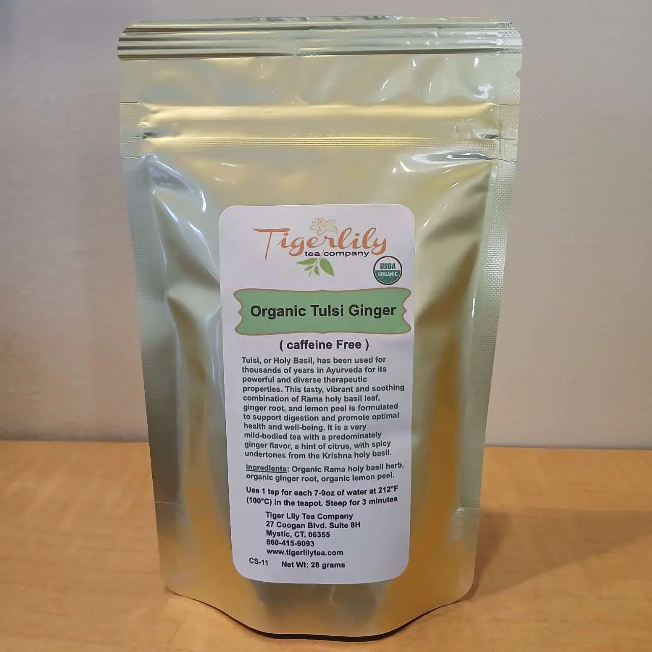 Tigerlily Organic Tulsi Ginger tea package on a wooden surface with a white background