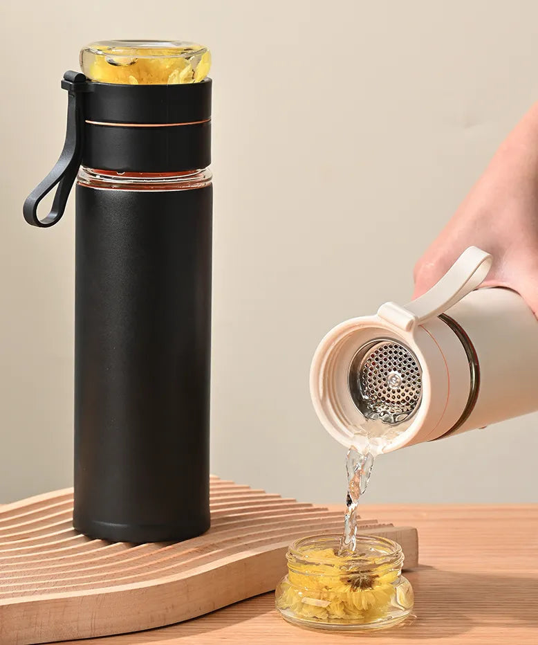 Black glass travel mug with a hand pouring water into a small glass container on a wooden surface.