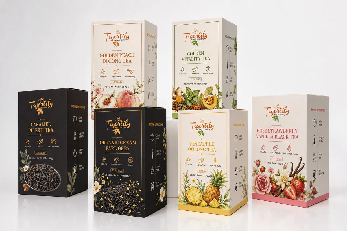 Six boxes of TeaKitty tea arranged on a clean white studio background. The set includes black boxes for Caramel Pu-Erh Tea and Organic Cream Earl Grey Tea, and cream/white boxes for Golden Peach Oolong Tea, Golden Vitality Tea, Pineapple Oolong Tea, and Rose Strawberry Vanilla Black Tea.